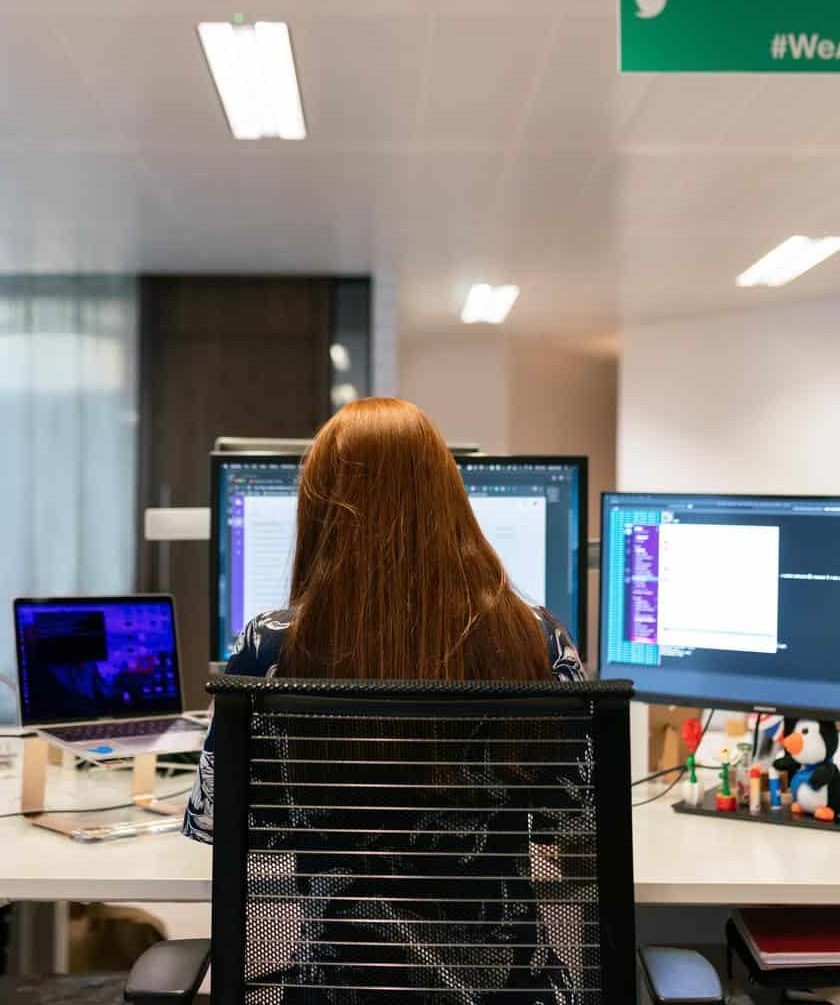 Red haired woman with her back to the camera working on a PC