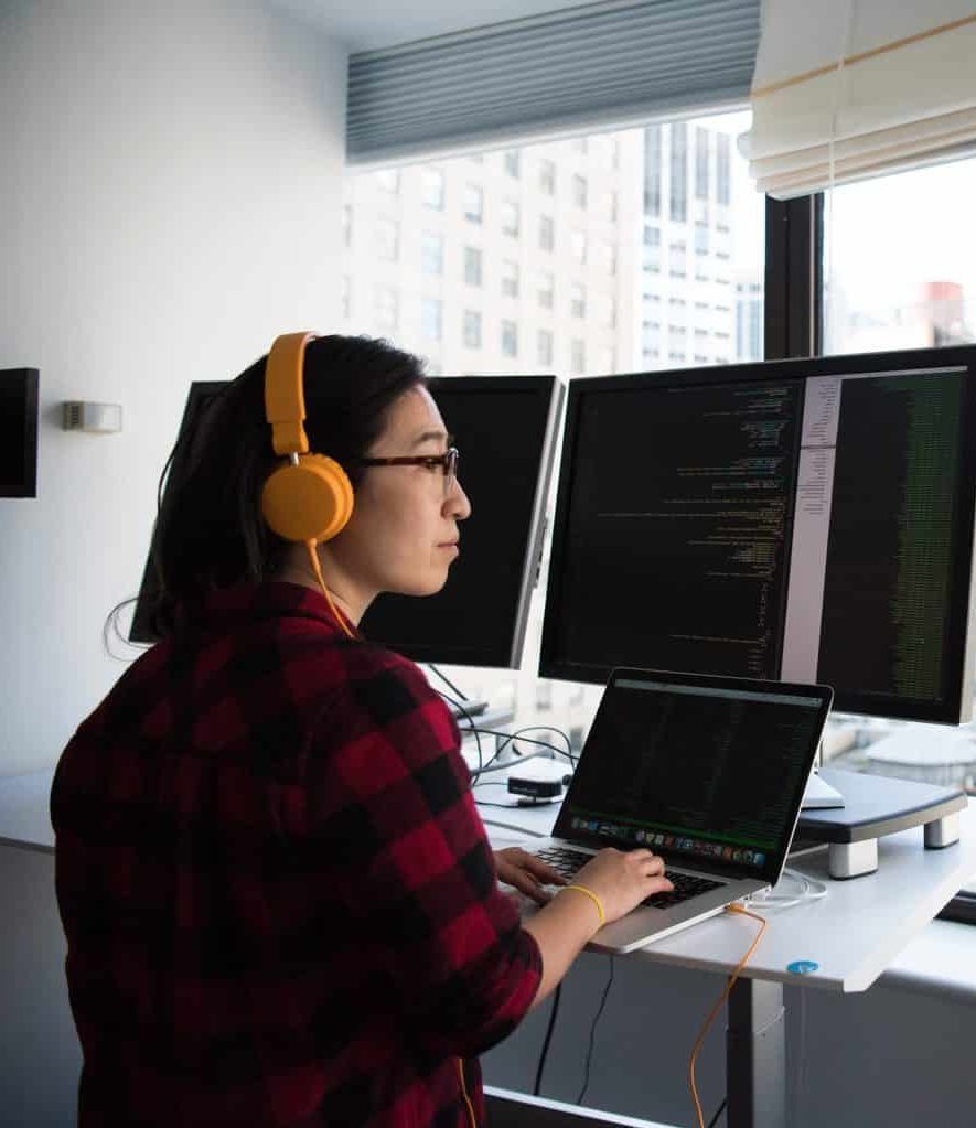 Woman in IT security working with multiple monitors with her back to the camera