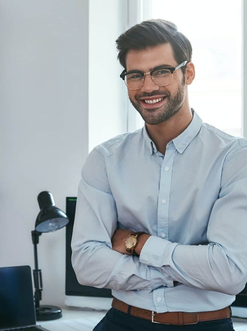 Happy trader. Cheerful businessman in formal clothes and eyeglasses is keeping arms crossed, smiling