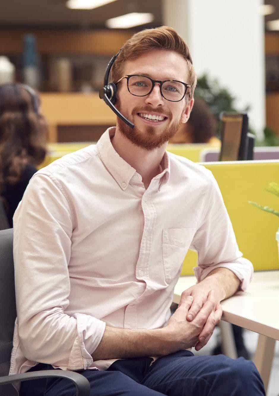 Portrait Of Businessman Wearing Headset Talking To Caller In Customer Services Centre
