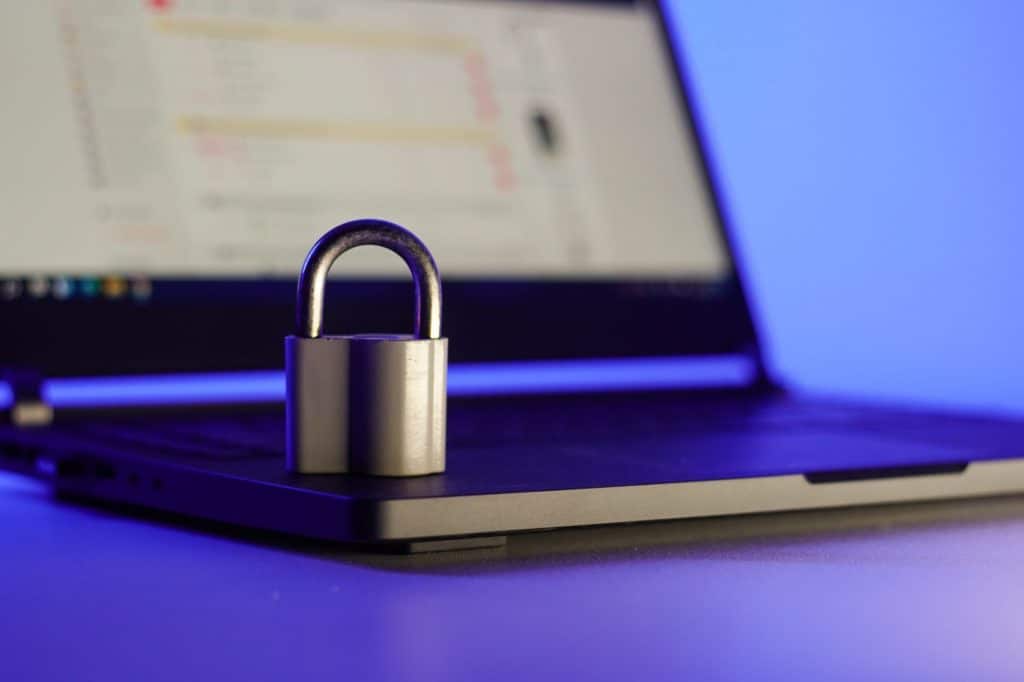 Locked metal padlock on a laptop keyboard over blue background. Cyber security concept.