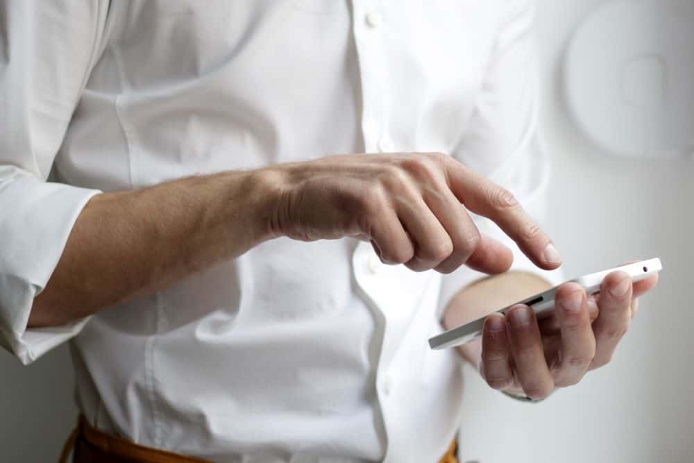 Man in white shirt typing on a white mobile phone