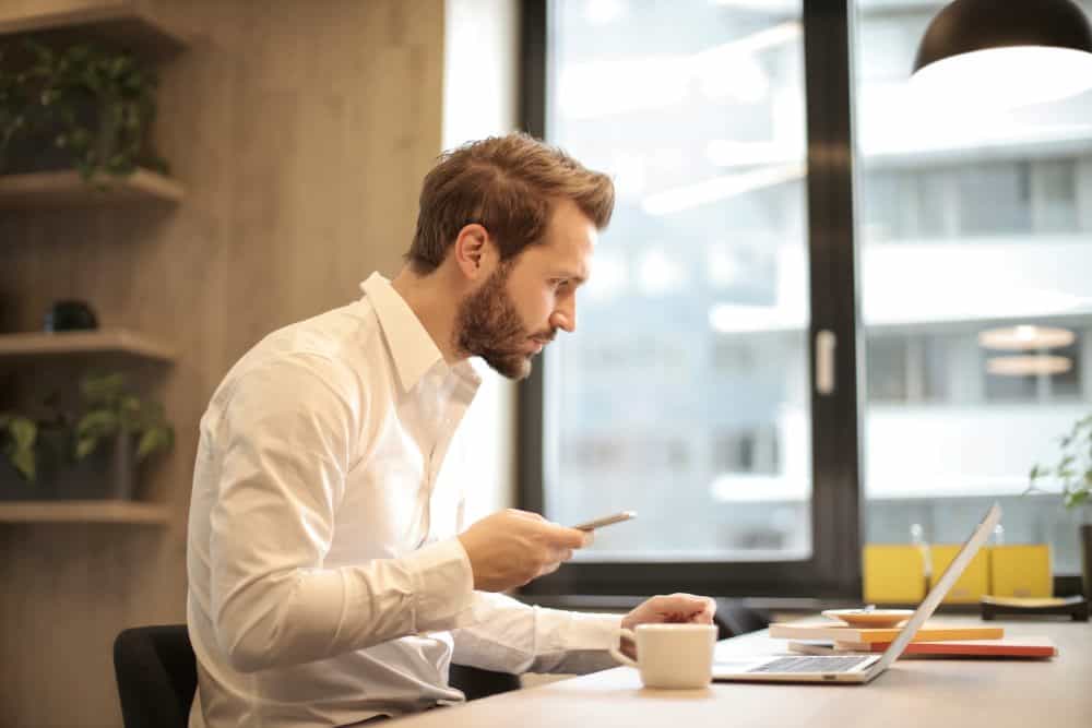 Man in shirt using mobile phone on laptop